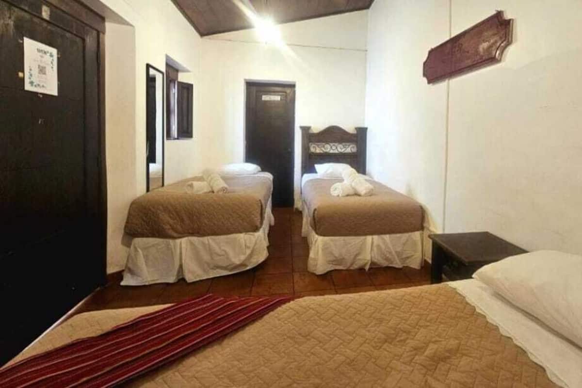 A room with two single beds, a wooden door, a small table, and a red rug.
