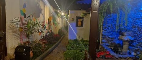 A corridor with a tiled floor, potted plants, and a wall with colorful artwork.