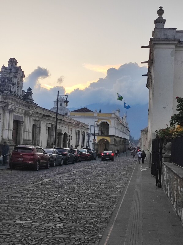 Een geplaveid straatje met historische gebouwen, een vlag en geparkeerde auto's.