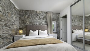 A bedroom with a stone wall, a bed with white bedding, a beige throw blanket, and a nightstand with a lamp. - Villa Angelica with heated pool (Kvarner - Lakmartin) (Lakmartin)