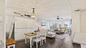A spacious living area with a dining table, white furniture, and a view of the outdoors through large windows. - SeaCrest ~N Forest Beach Coligny OCEANVIEW~HUGE 1 bedroom!  Top floor! POOL! Gym (Hilton Head Island)