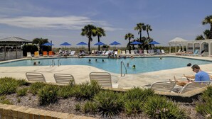 A pool area with multiple lounge chairs and umbrellas, surrounded by palm trees and a clear sky. - SeaCrest ~N Forest Beach Coligny OCEANVIEW~HUGE 1 bedroom!  Top floor! POOL! Gym (Hilton Head Island)