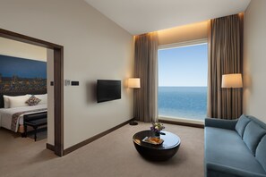 Un cuarto de hotel con cama, sofá, mesa de centro, televisión y vista al mar.