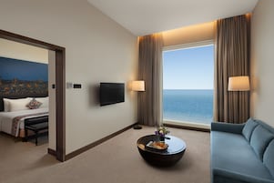 Un cuarto de hotel con cama, sofá, mesa de centro, televisión y vista al mar.