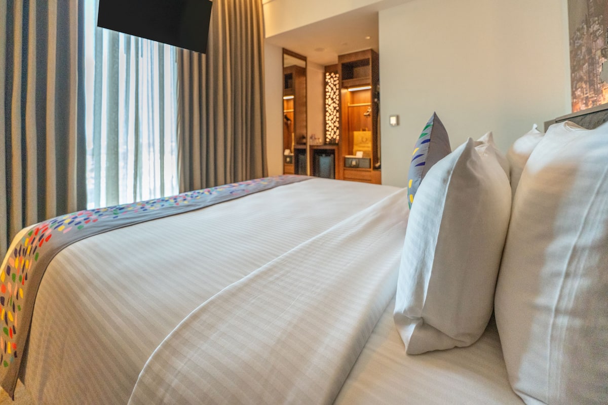 A hotel room with a large bed, a TV mounted on the wall, and a bathroom visible through an open door.