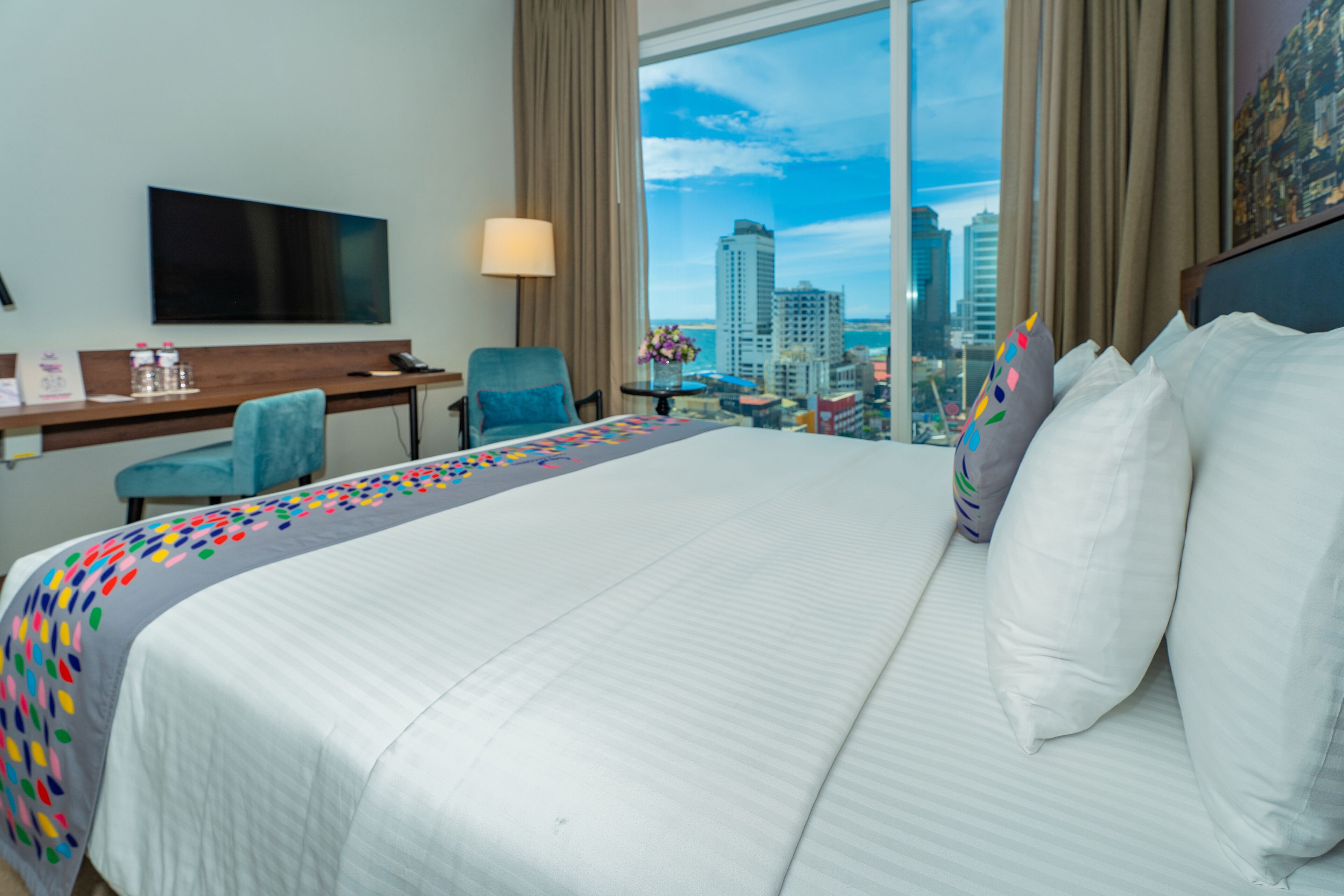 Une chambre d’hôtel avec un grand lit, un bureau, une chaise, une télévision et une vue sur le paysage urbain.