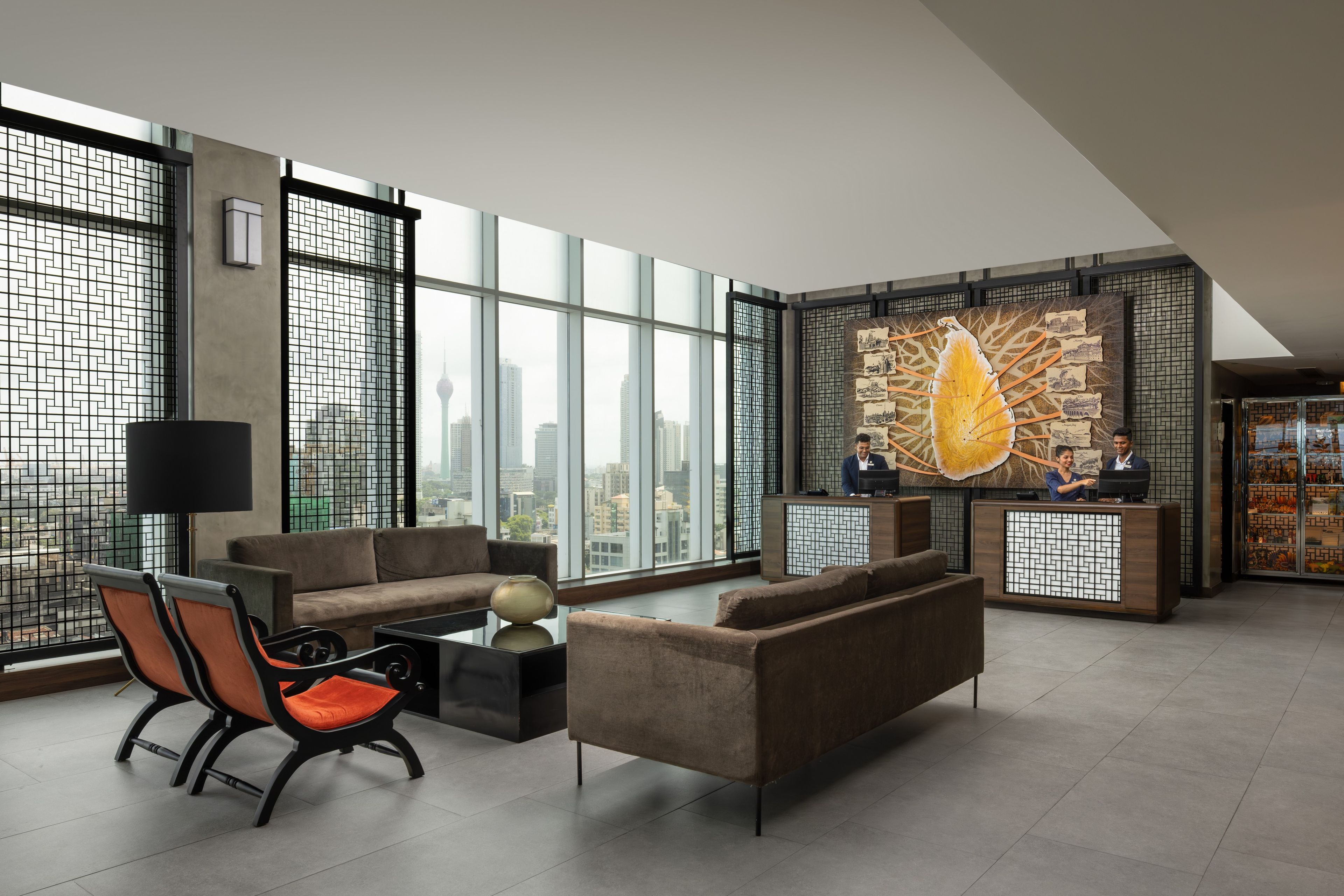 A modern hotel lobby with a reception desk, seating area, and large windows offering city views.