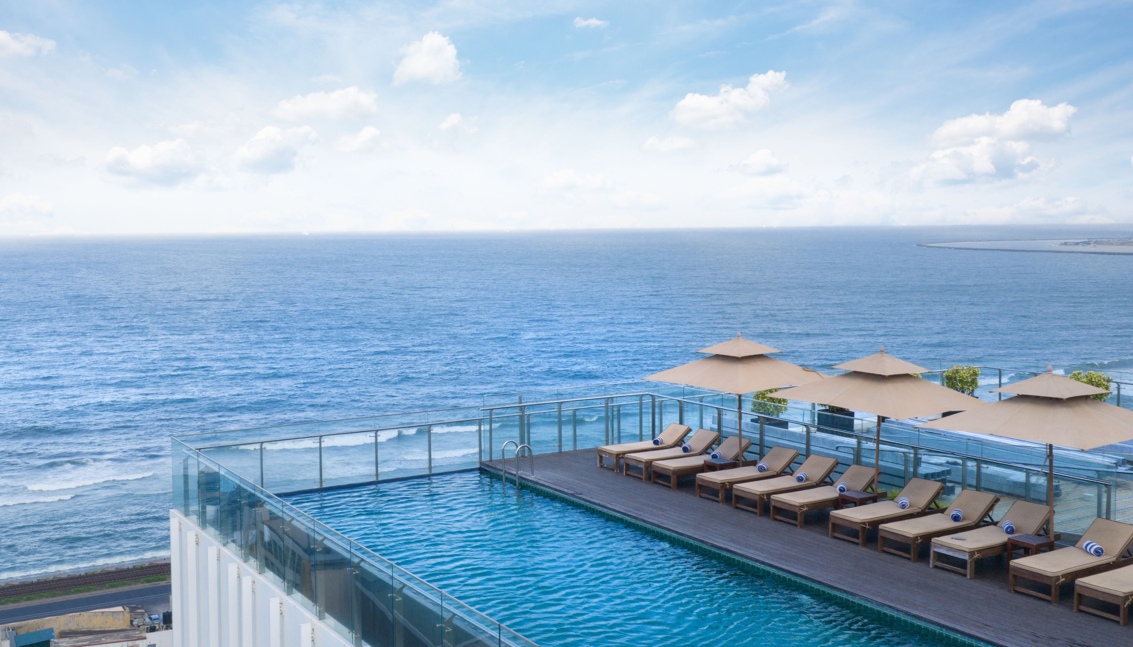 Una piscina infinita en la azotea con sillones y sombrillas, con vistas al océano.