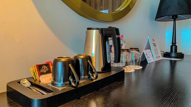 A hotel room's minibar with a coffee maker, two cups, a spoon, and a bottle of water. - Sofia Colombo City Hotel (Colombo)