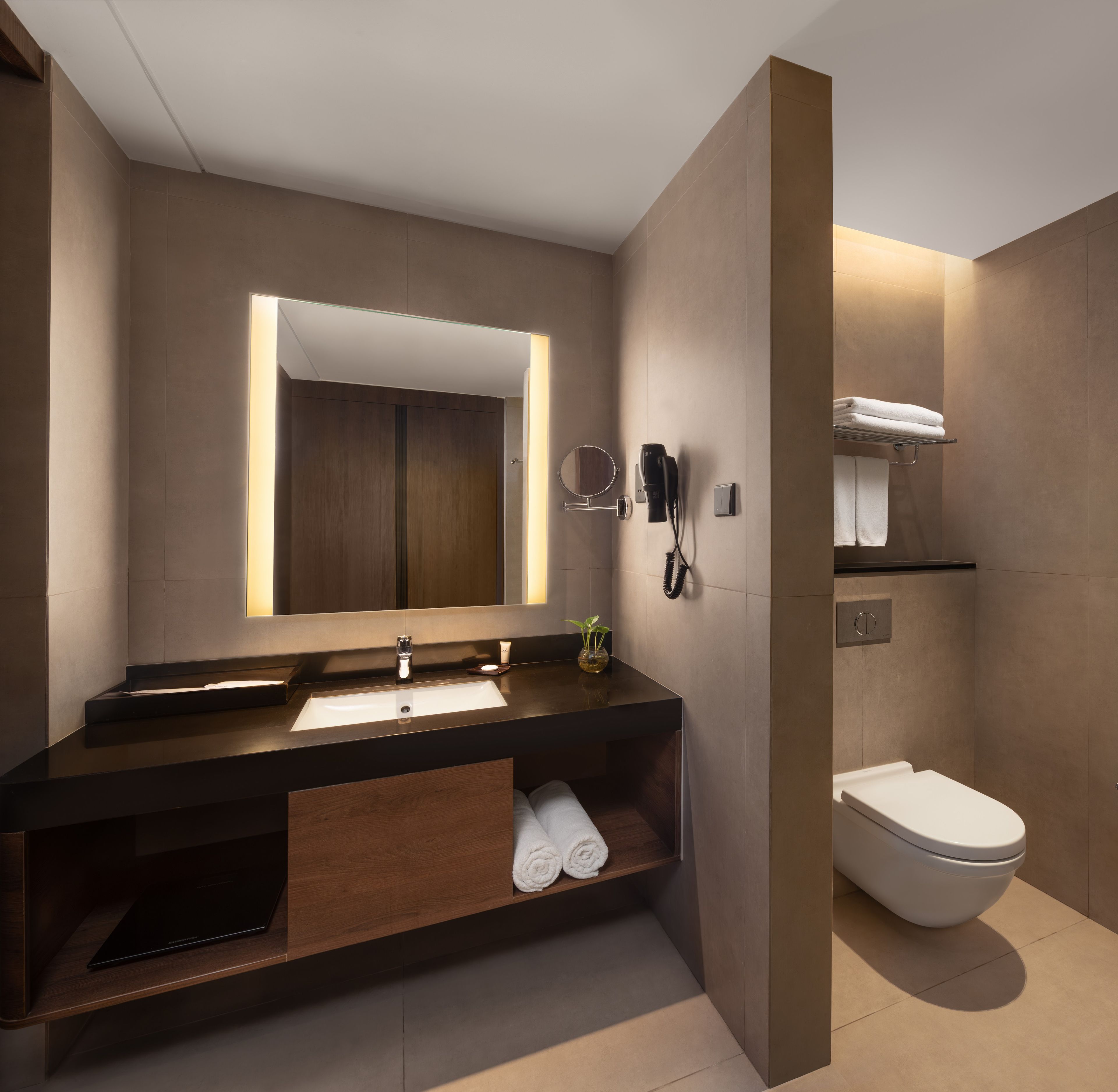 A modern bathroom with a dark wood vanity, a large mirror, a hairdryer, and a toilet.