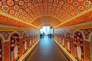 Um corredor com decoração detalhada nas paredes e no teto, que dá para uma vista de edifícios lá fora.