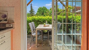 A patio with a table and chairs, a glass door, and a view of greenery. - Flaschenpost by Interhome (Zinnowitz)