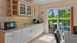 A kitchen with a microwave, sink, and cabinets, a dining area with a table and chairs, and a sliding glass door leading to a patio with greenery. - Flaschenpost by Interhome (Zinnowitz)