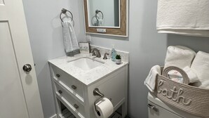 A bathroom with a white sink, mirror, and toilet. There is a towel rack with a towel, a small plant, and a soap dispenser on the sink.