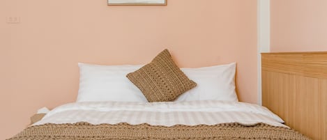 Uma cama com roupa de cama branca e um cobertor de malha castanho, uma obra de arte emoldurada acima, e uma cabeceira de madeira.