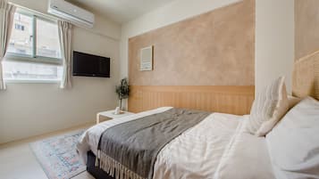 A bedroom with a bed, a bedside table with a plant, a wall-mounted TV, and an air conditioning unit.