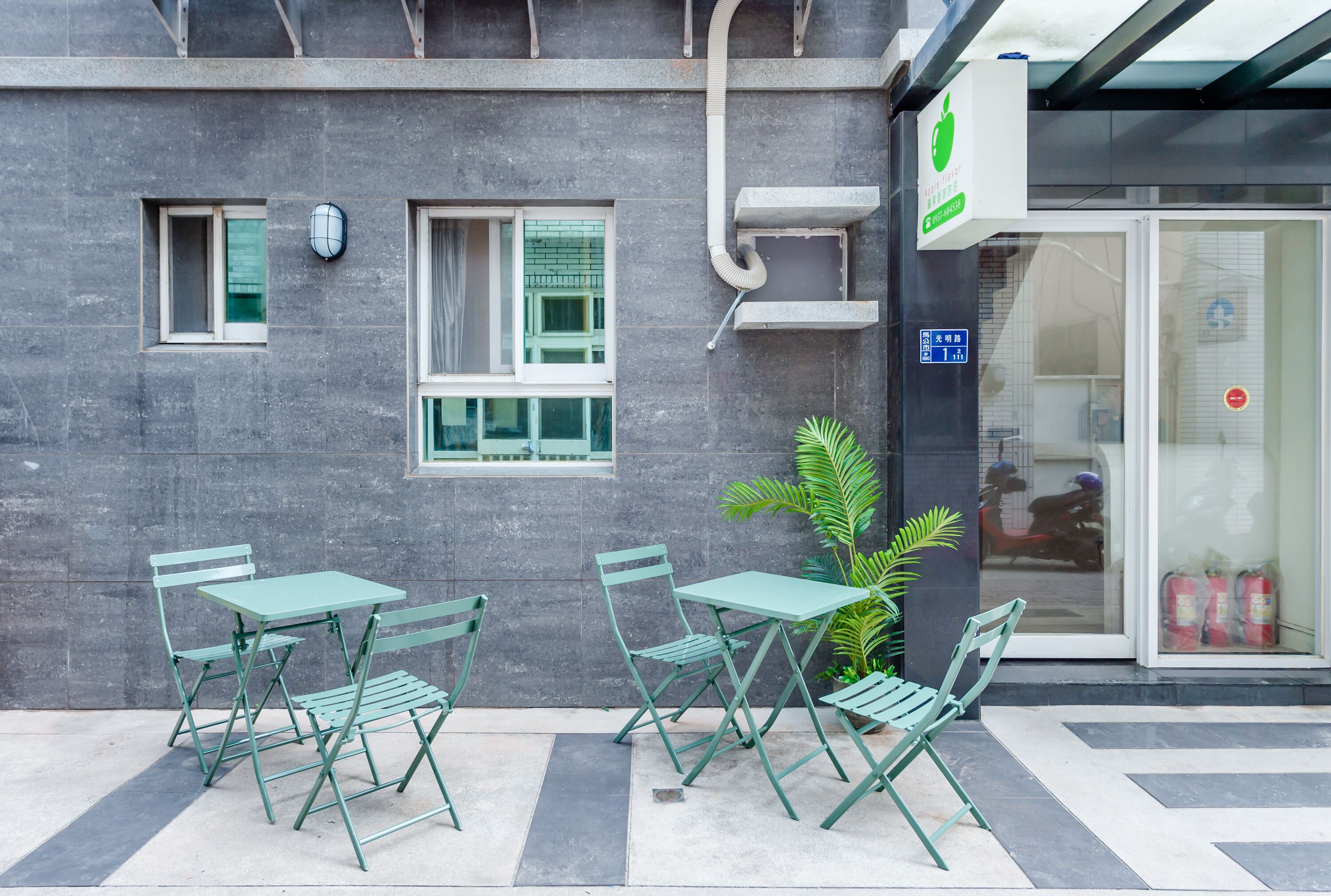 A building exterior with a green outdoor seating area, a fire extinguisher, and a sign indicating a business.