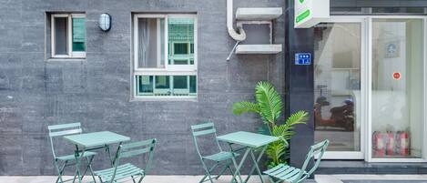 Fachada de un edificio con un área de estar exterior verde, un extintor y un letrero que indica que se trata de un negocio.