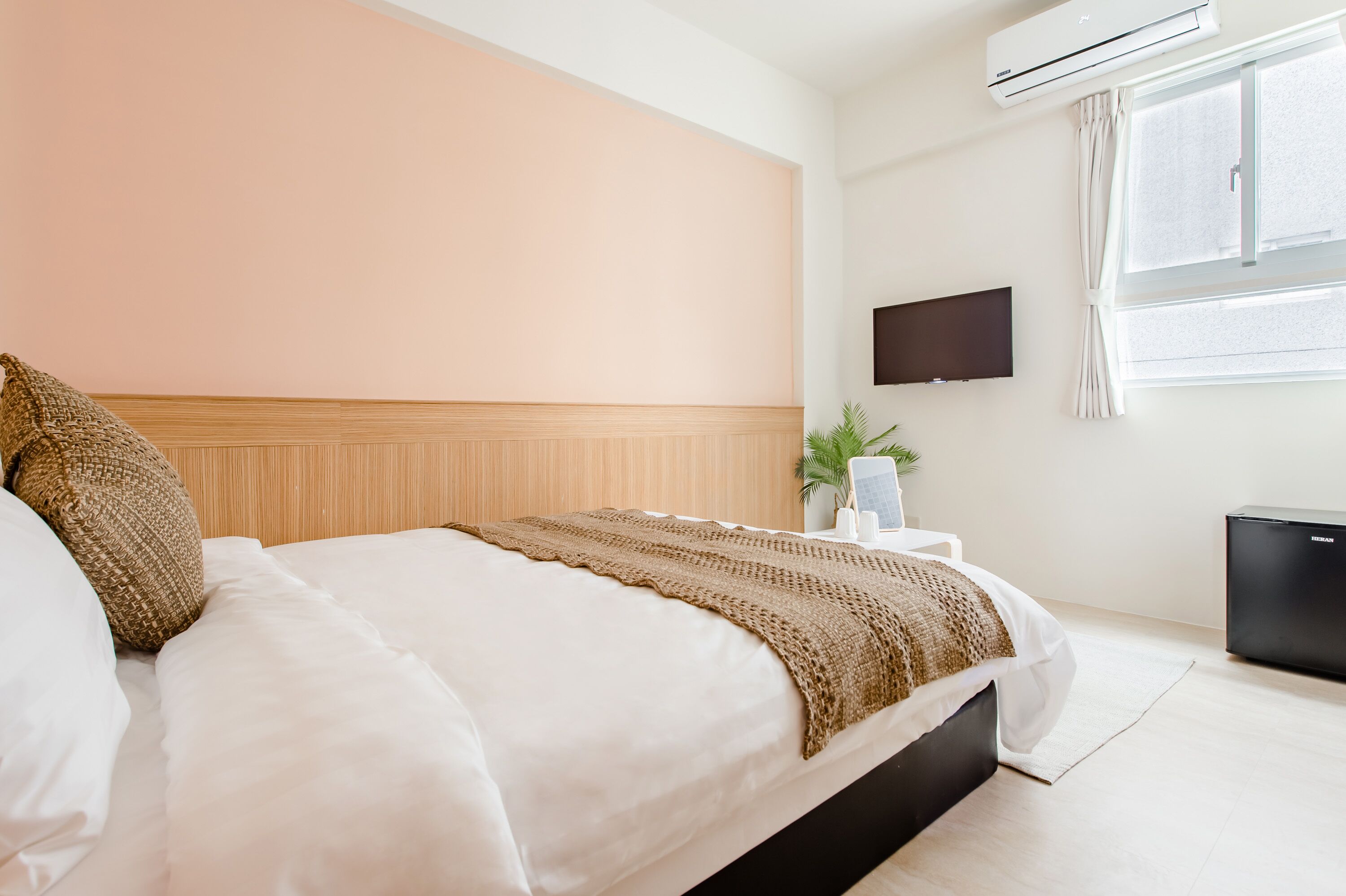 Habitación de hotel con cama, televisor de pantalla plana montado en la pared, ventana con cortinas y un refrigerador negro pequeño.
