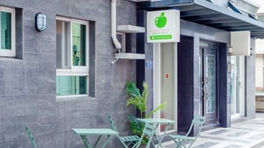 A building with a green sign, outdoor seating, and a potted plant. - Apple Scent Easy Stay (Magong)