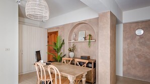A dining area with a wooden table and chairs, a pendant light, a potted plant, and a shelf with decorative items. - Apple Scent Easy Stay (Magong)