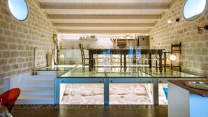 Um quarto amplo com mesa e cadeiras de vidro, paredes de pedra e teto de madeira.