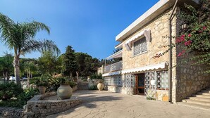 A stone building with a balcony, a large potted plant, and a garden with various plants and flowers.