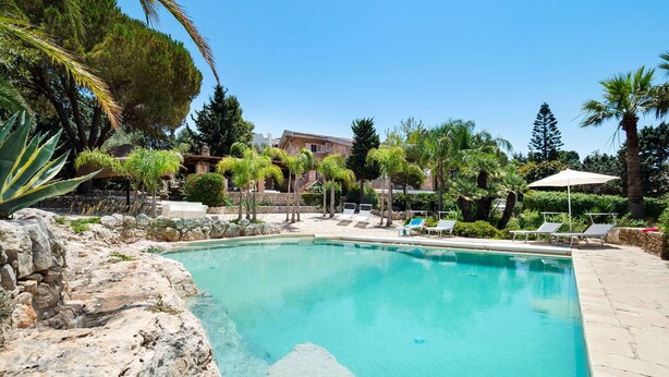 A swimming pool surrounded by lounge chairs and palm trees.