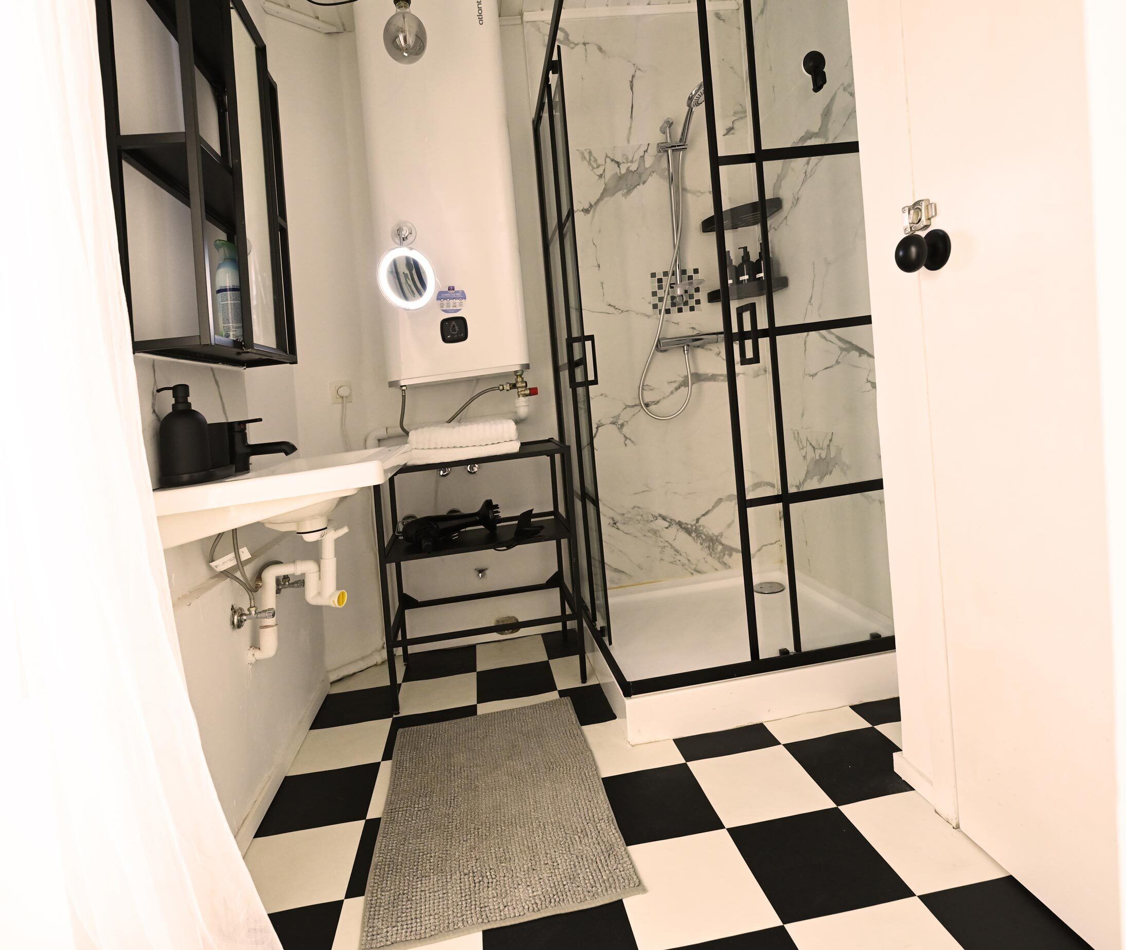 Een badkamer met een zwart-wit geruite vloer, een glazen douchecabine, een wit wastafelmeubel, een spiegel en een handdoekhouder.