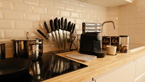 Una cocina con estufa negra, una olla, cafetera y un bloque de cuchillos.