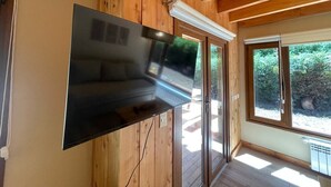 Een modern interieur met een flatscreen televisie, bevestigd aan een houten wand, grote ramen en een houten plafond.