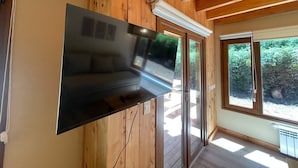 Een modern interieur met een flatscreen televisie, bevestigd aan een houten wand, grote ramen en een houten plafond.