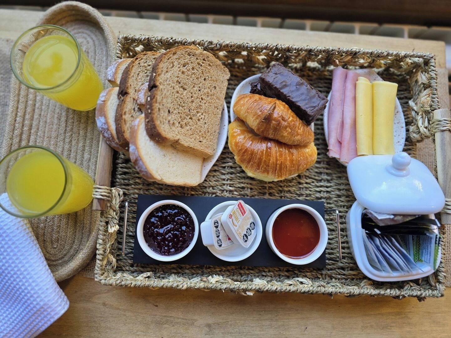 Bandeja de desayuno con pan, croissants, jamón, queso y salsas.