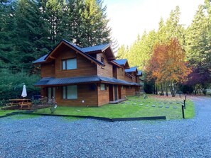 Situated in a forested area, this cabin features a front porch with a bench and table, perfect for relaxation or dining.