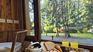 A breakfast tray with bread, pastries, and beverages on a table by a window with a view of a forest. - Remanso del Bosque - Los Teros Cabin (Puerto Manzano)
