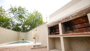 A modern outdoor area with a swimming pool, a barbecue grill, and a small garden with pampas grass.