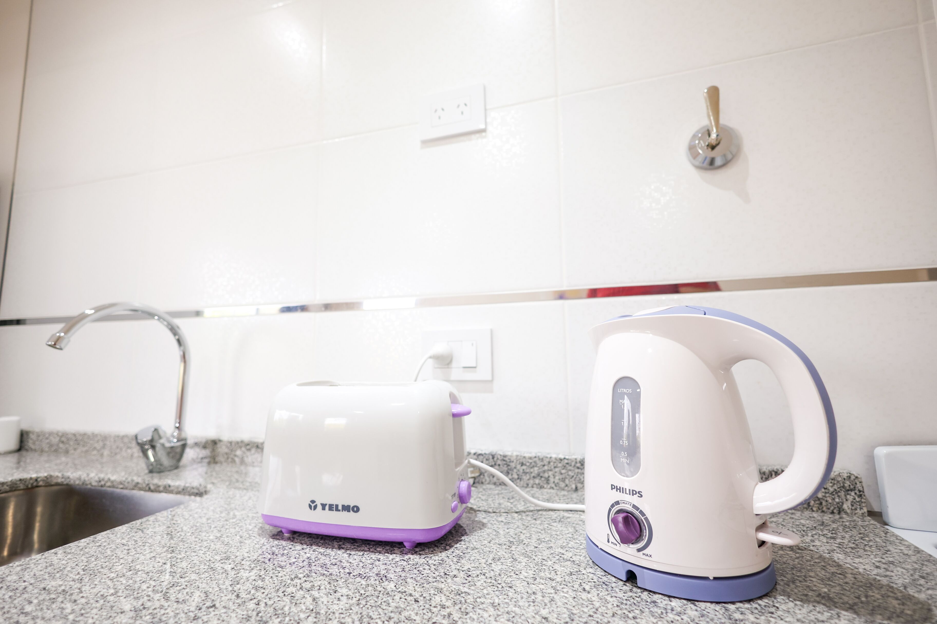 A kitchen with a granite countertop, a white and purple toaster, and a white and blue kettle.