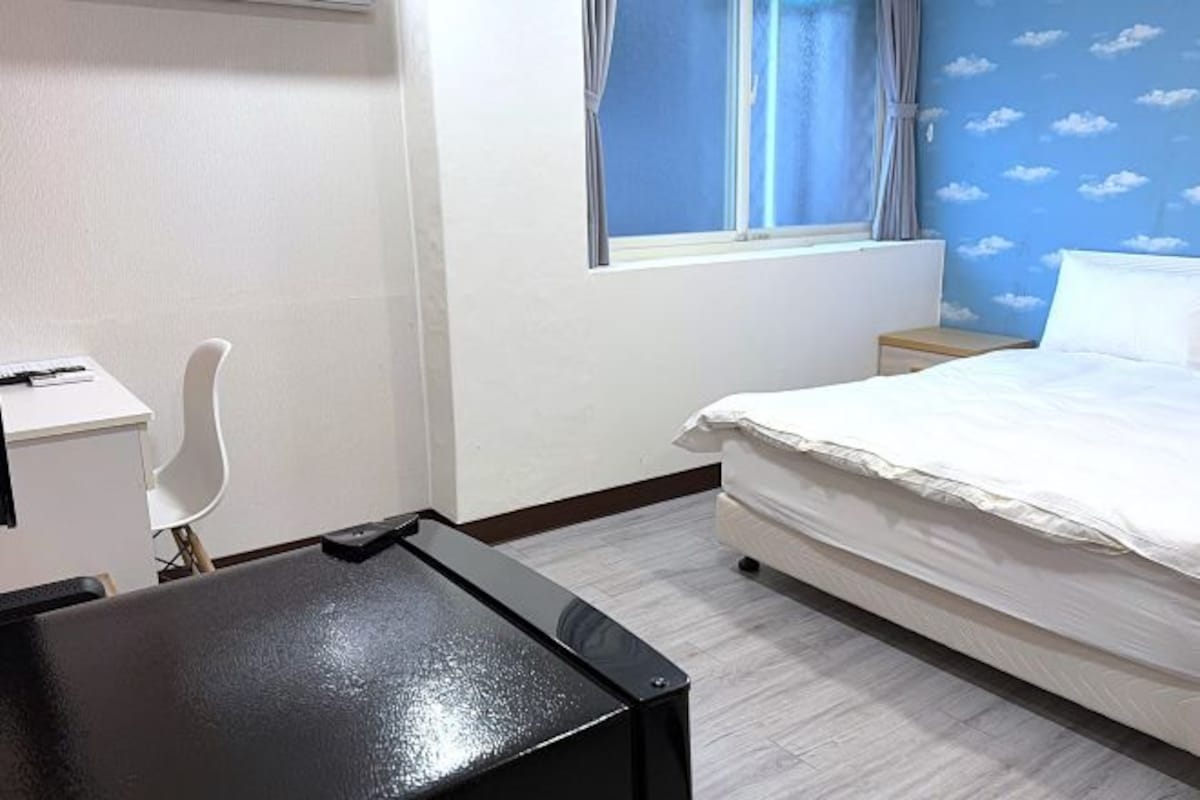 A hotel room with a bed, a desk, a chair, and a window with curtains.