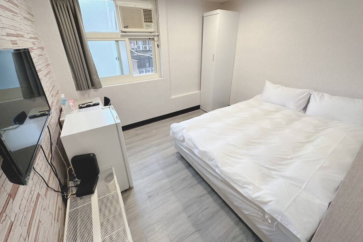 Een hotelkamer met een bed, een bureau met een computer, een televisie en een raam met gordijnen.