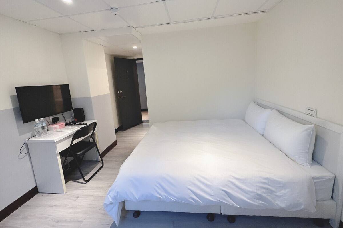 Een hotelkamer met een bed, een bureau met een computer, een flatscreen televisie en een deur die leidt naar een andere kamer.