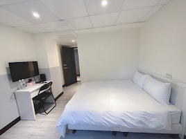 A hotel room with a bed, a desk with a computer, a flat-screen TV, and a door leading to another room.