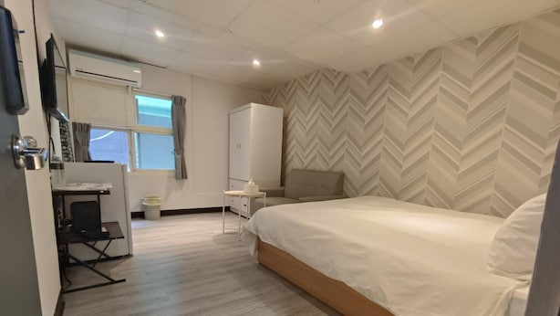 Een moderne hotelkamer met een groot bed, een bureau met stoel, een kledingkast en een wand met een herringbone-patroon.