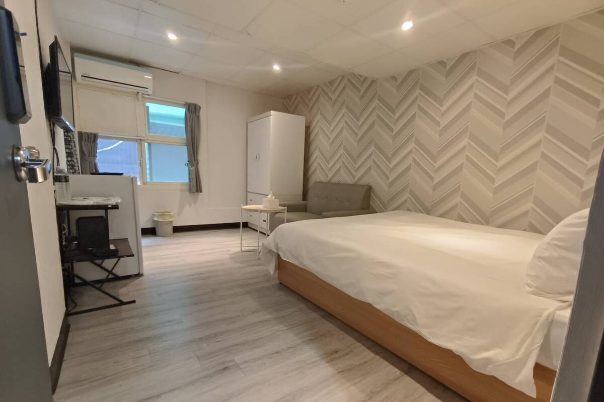 Een moderne hotelkamer met een groot bed, een bureau met stoel, een kledingkast en een wand met een herringbone-patroon.