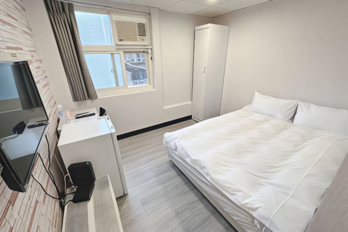 A hotel room with a bed, a desk, a wardrobe, and a window with curtains.