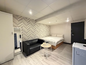 Quarto de hotel pequeno com uma cama, um sofá preto, uma mesinha redonda e um guarda-roupa.