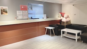 Een hotel receptie met een balie, een spiegel, een teddybeer en een tafeltje.