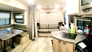 A compact RV interior with a kitchenette, a dining area, and a seating space. - The Magnolia House RV Winnebago Sleeps 3 (Lakeview)