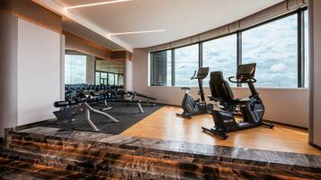A modern gym with exercise equipment, large windows, and a marble staircase.