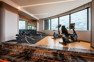 A modern gym with exercise equipment, large windows, and a marble staircase.