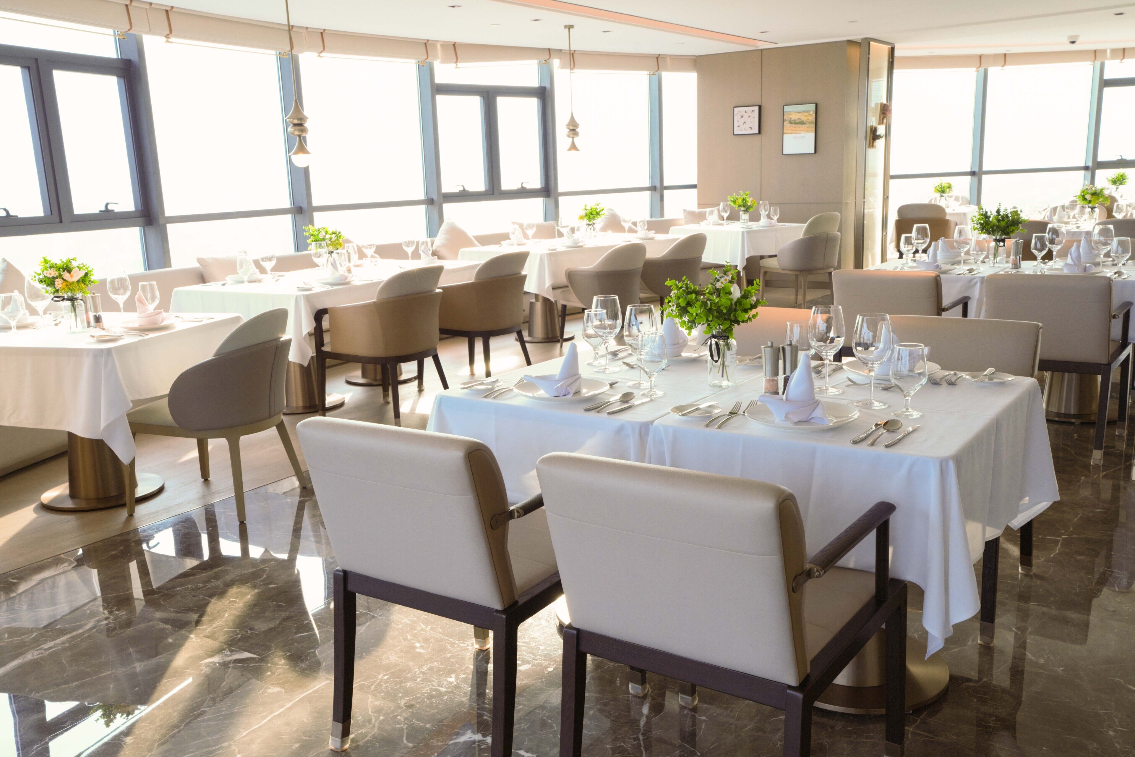 Un ristorante con diversi tavoli apparecchiati, ampie finestre e un design interno moderno.